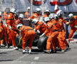 Oamenii în salopete portocalii îndepărtează de pe pistă în viteză, folosind inclusiv mături, resturile maşinii lui Maldonado // Foto: Reuters