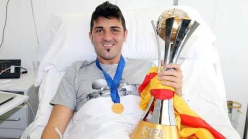 David Villa pe patul spitalului, după operaţie, şi cu medalia de campion şi trofeul acordat Barcelonei pentru cîştigarea CM al cluburilor