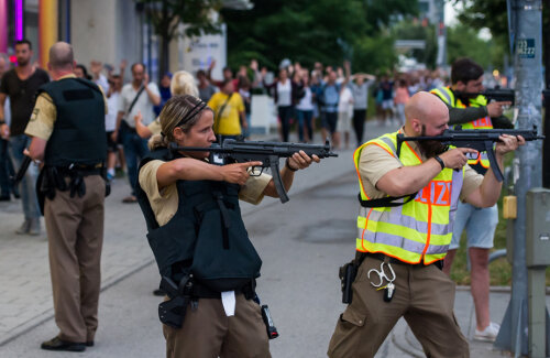 Polițiștii țintesc cu armele automate, în timp ce oamenii trec speriați prin spatele lor // FOTO Guliver/GettyImages